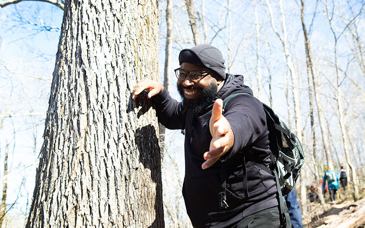 Man leaning against a tree holding out hand. Visit outdoorafro.org